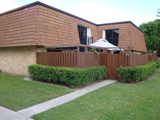 view of property exterior with mansard roof, a lawn, fence, and brick siding