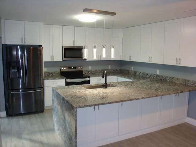 kitchen featuring light wood-style floors, appliances with stainless steel finishes, a peninsula, stone counters, and a sink