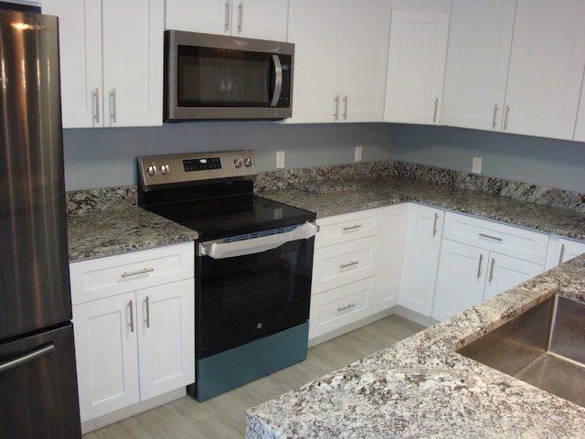 kitchen with stainless steel appliances, light wood finished floors, stone counters, and white cabinets