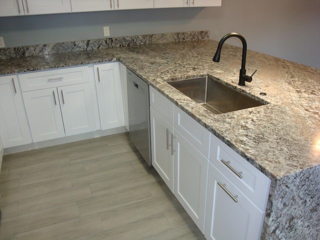 kitchen featuring dishwashing machine, light stone counters, a sink, and white cabinetry