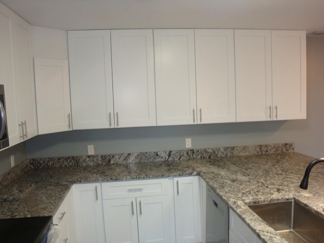 kitchen featuring dishwasher, a sink, light stone countertops, and white cabinets