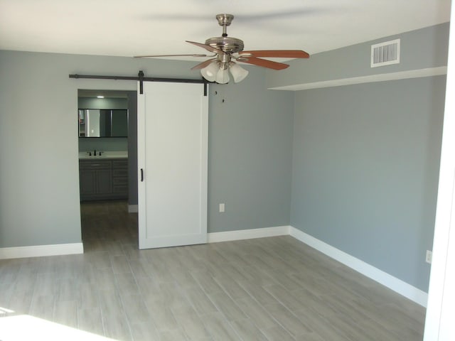 spare room with a barn door, wood finished floors, visible vents, and baseboards