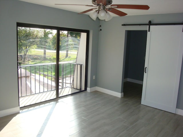 unfurnished room featuring ceiling fan, a barn door, wood finished floors, and baseboards