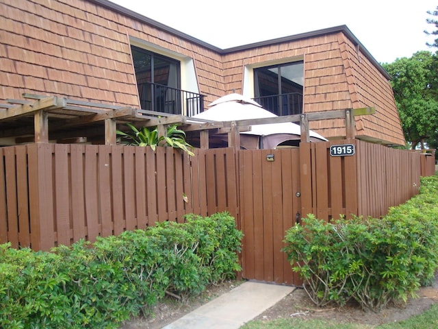 view of side of home featuring mansard roof, fence, and a balcony