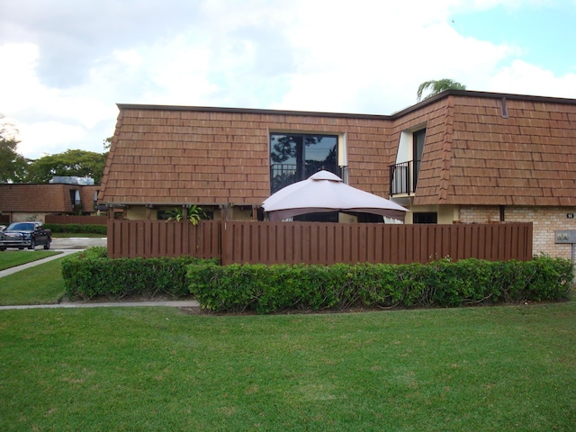 view of home's exterior featuring mansard roof, a lawn, fence, and brick siding