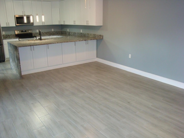 kitchen featuring stainless steel appliances, dark stone counters, white cabinetry, and light wood-style flooring