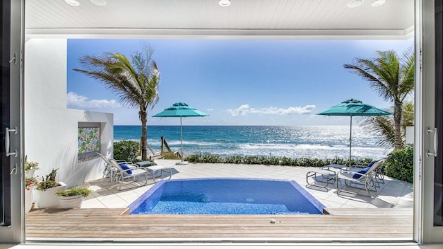 view of swimming pool with a water view, a view of the beach, and a hot tub