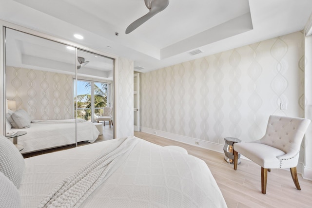 bedroom featuring wallpapered walls, a tray ceiling, baseboards, and visible vents