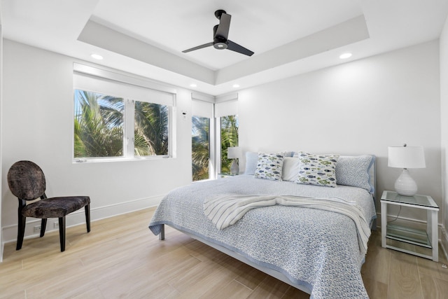 bedroom featuring baseboards, a raised ceiling, and light wood-style floors