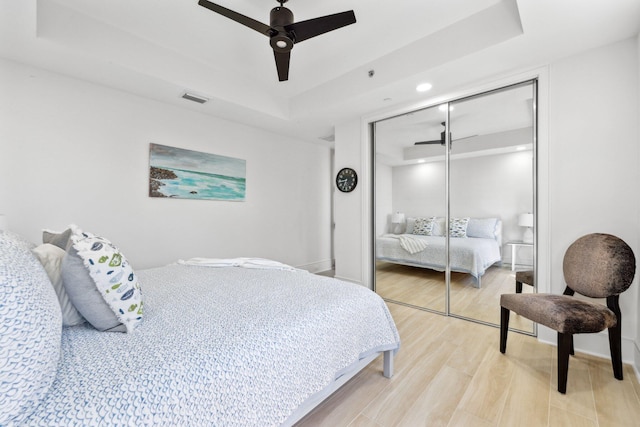 bedroom featuring a ceiling fan, visible vents, a tray ceiling, a closet, and light wood-type flooring