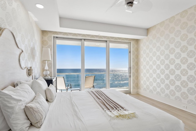 bedroom featuring wallpapered walls, ceiling fan, a water view, baseboards, and wood finished floors