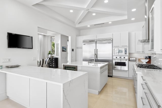 kitchen featuring built in appliances, recessed lighting, a peninsula, coffered ceiling, and a kitchen island with sink