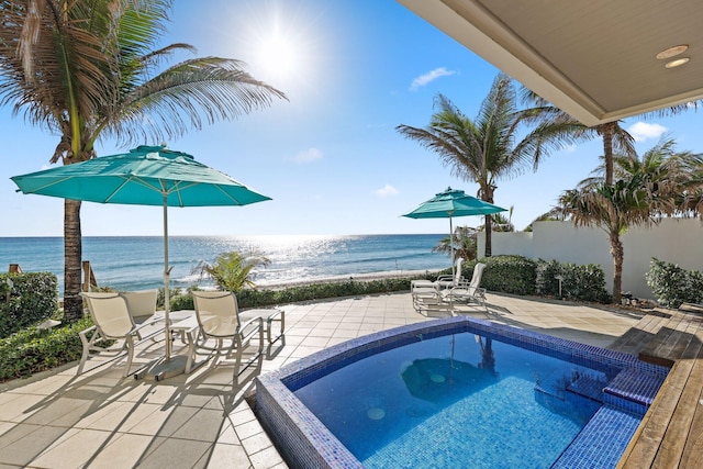 view of pool featuring a patio, a beach view, fence, and a water view