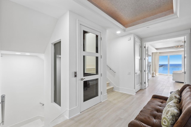 living area with a tray ceiling, light wood-style flooring, stairway, and baseboards