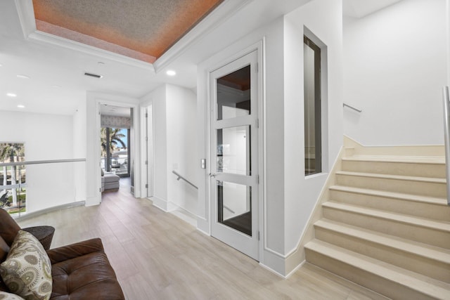 hallway with light wood-type flooring, visible vents, a tray ceiling, stairway, and baseboards