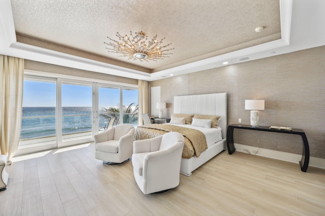 bedroom with an inviting chandelier, a tray ceiling, access to outside, and light wood finished floors