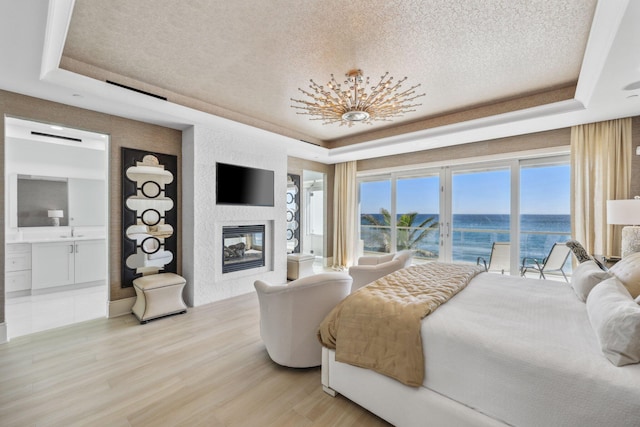 bedroom with a tray ceiling, light wood-style floors, and access to outside