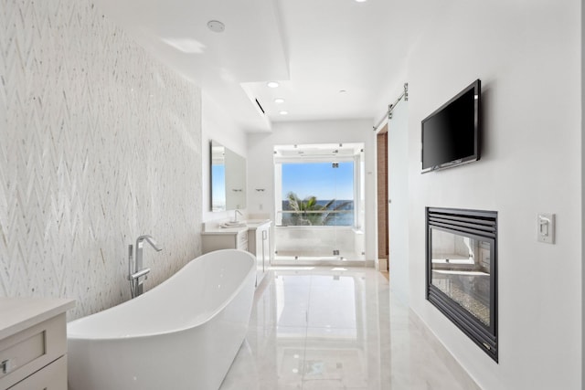 bathroom with vanity, a freestanding tub, recessed lighting, a glass covered fireplace, and marble finish floor