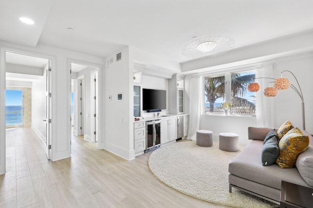 living area with light wood-style floors, beverage cooler, visible vents, and baseboards