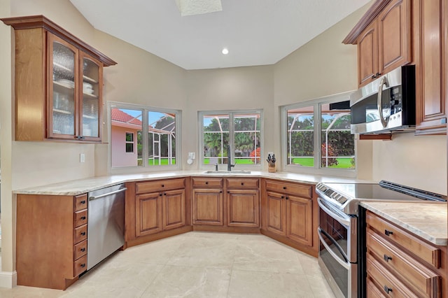 kitchen with appliances with stainless steel finishes, brown cabinets, a sink, and glass insert cabinets