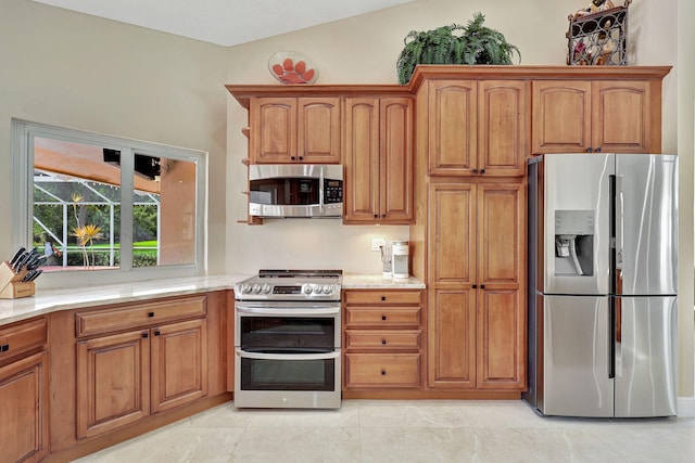 kitchen featuring vaulted ceiling, appliances with stainless steel finishes, brown cabinets, and light stone counters