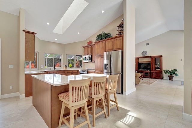 kitchen featuring a skylight, a sink, a kitchen island, appliances with stainless steel finishes, and brown cabinets