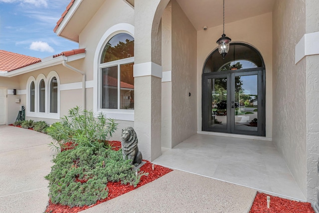 view of exterior entry featuring stucco siding, a tiled roof, and french doors