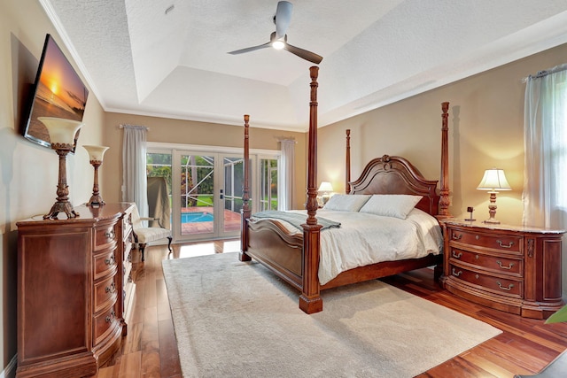 bedroom with ceiling fan, wood finished floors, access to exterior, a tray ceiling, and a textured ceiling