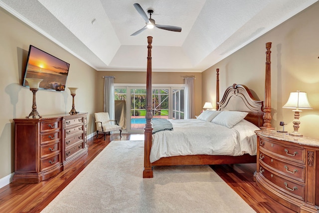 bedroom featuring baseboards, ceiling fan, wood finished floors, access to outside, and a tray ceiling