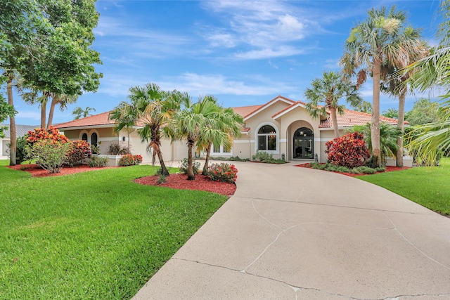 mediterranean / spanish home featuring concrete driveway, a tile roof, a front lawn, and stucco siding