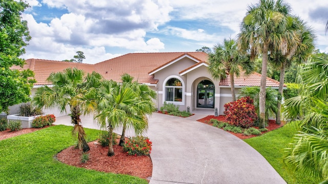 mediterranean / spanish-style house with concrete driveway, a tiled roof, french doors, stucco siding, and a front yard