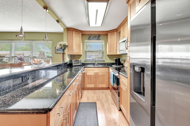 kitchen featuring light wood-style flooring, stainless steel appliances, a textured ceiling, light brown cabinetry, and a sink