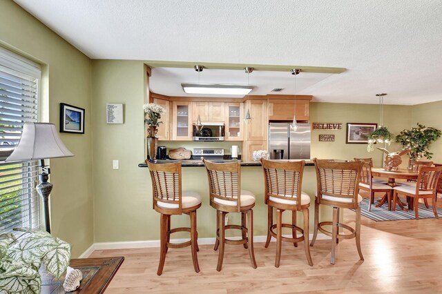 kitchen with stainless steel appliances, a peninsula, light brown cabinets, and visible vents