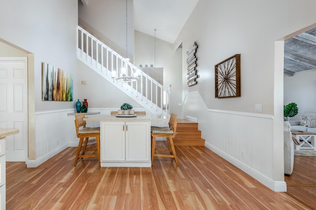 interior space with wainscoting, stairway, light wood-type flooring, and a towering ceiling