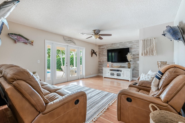 living area featuring light wood-style flooring, ceiling fan, a textured ceiling, and french doors