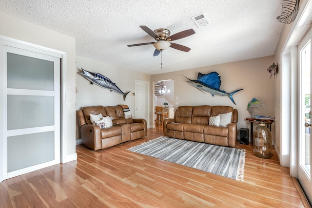 living room featuring a ceiling fan, visible vents, a textured ceiling, and wood finished floors