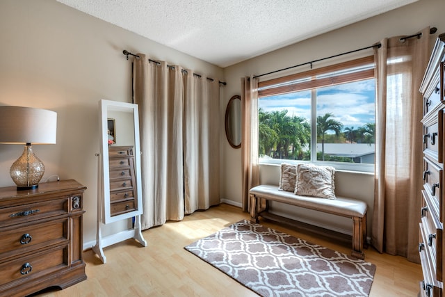 sitting room featuring light wood-type flooring, a textured ceiling, and baseboards