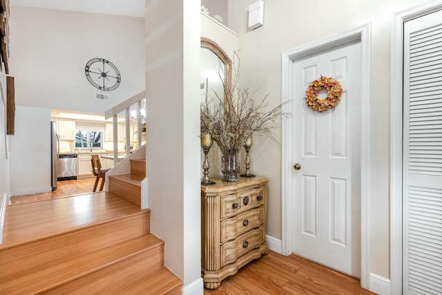 entryway with a high ceiling, light wood-style floors, stairs, and visible vents