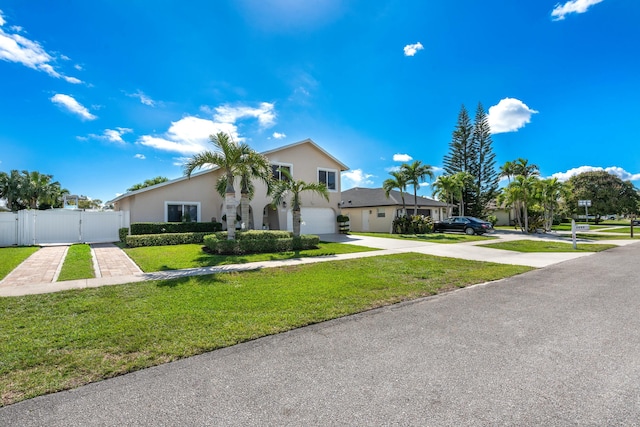 view of front of home with stucco siding, concrete driveway, a front yard, a gate, and fence