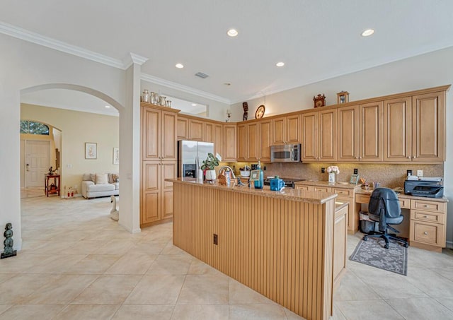 kitchen with arched walkways, stainless steel appliances, a kitchen island with sink, and decorative backsplash