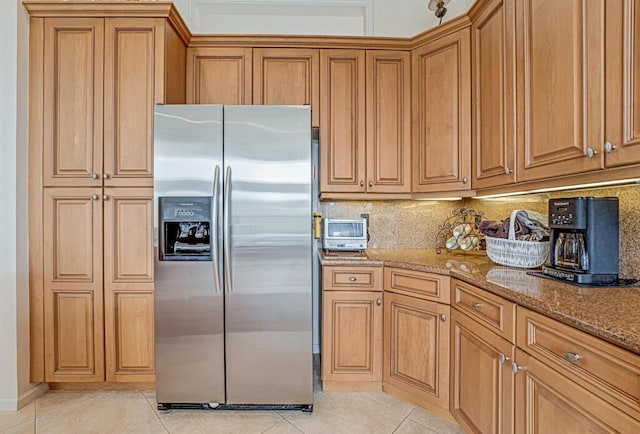 kitchen featuring tasteful backsplash, brown cabinetry, stainless steel fridge with ice dispenser, dark stone countertops, and light tile patterned flooring