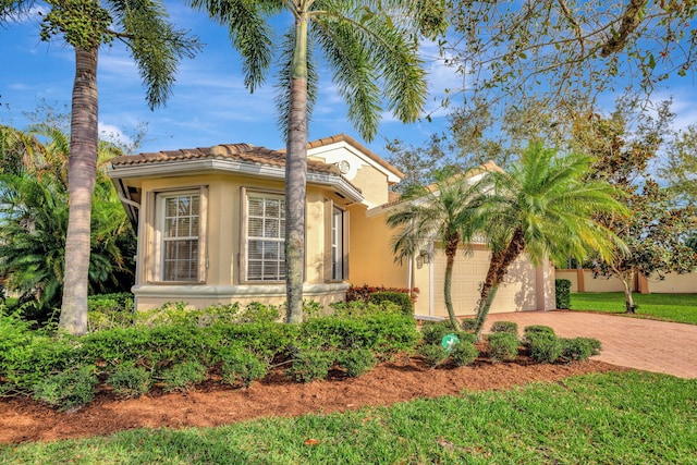 view of front facade featuring a garage, stucco siding, a tile roof, decorative driveway, and a front yard