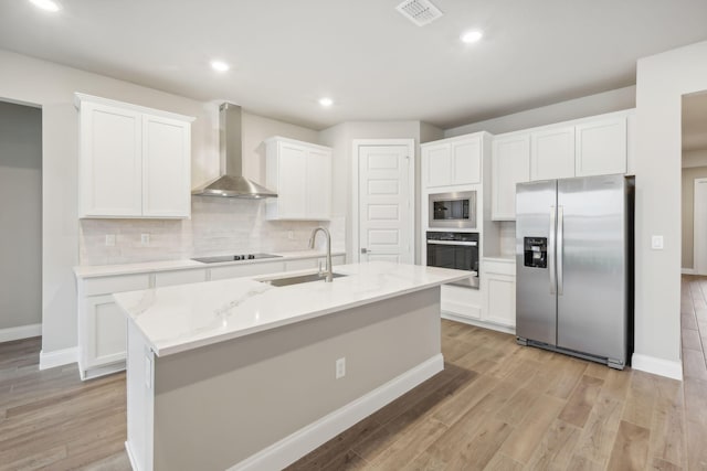 kitchen featuring visible vents, black appliances, a sink, white cabinets, and wall chimney range hood