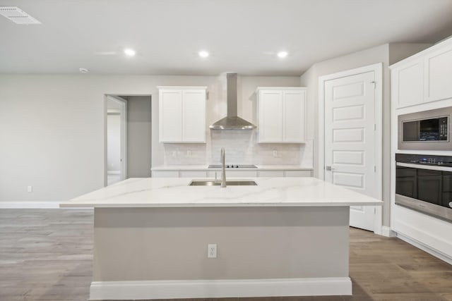 kitchen featuring oven, wall chimney range hood, an island with sink, decorative backsplash, and white cabinetry