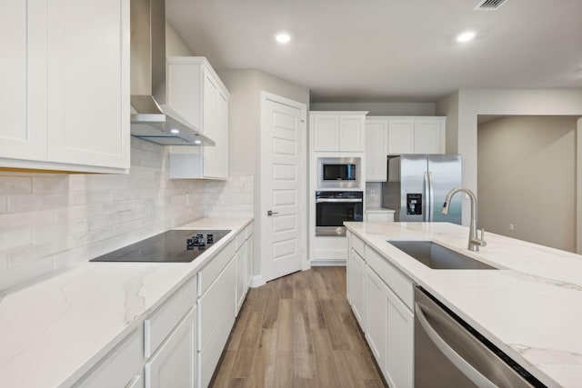 kitchen with a sink, light wood-style flooring, stainless steel appliances, wall chimney range hood, and white cabinets