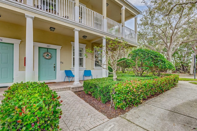 view of exterior entry featuring a balcony, a porch, and stucco siding