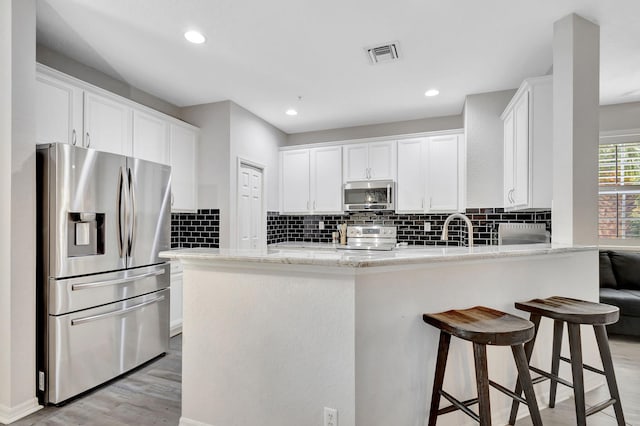 kitchen with visible vents, appliances with stainless steel finishes, white cabinetry, light wood-type flooring, and a peninsula