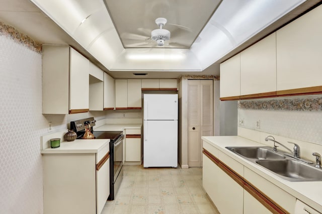 kitchen featuring freestanding refrigerator, a tray ceiling, light floors, a sink, and range with electric stovetop