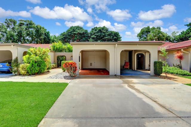 mediterranean / spanish-style house with concrete driveway, a front lawn, an attached carport, and stucco siding