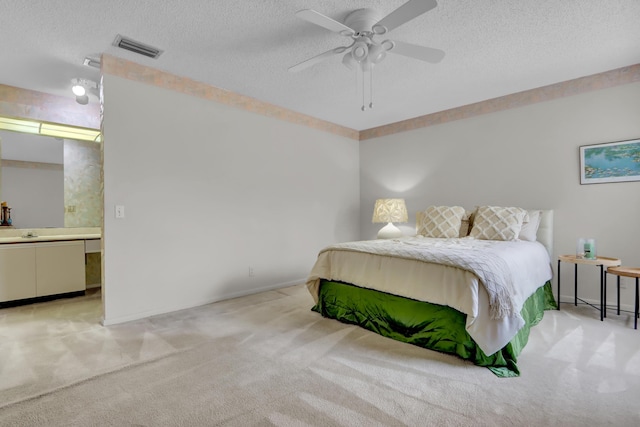 bedroom with visible vents, a ceiling fan, light colored carpet, ensuite bathroom, and a textured ceiling